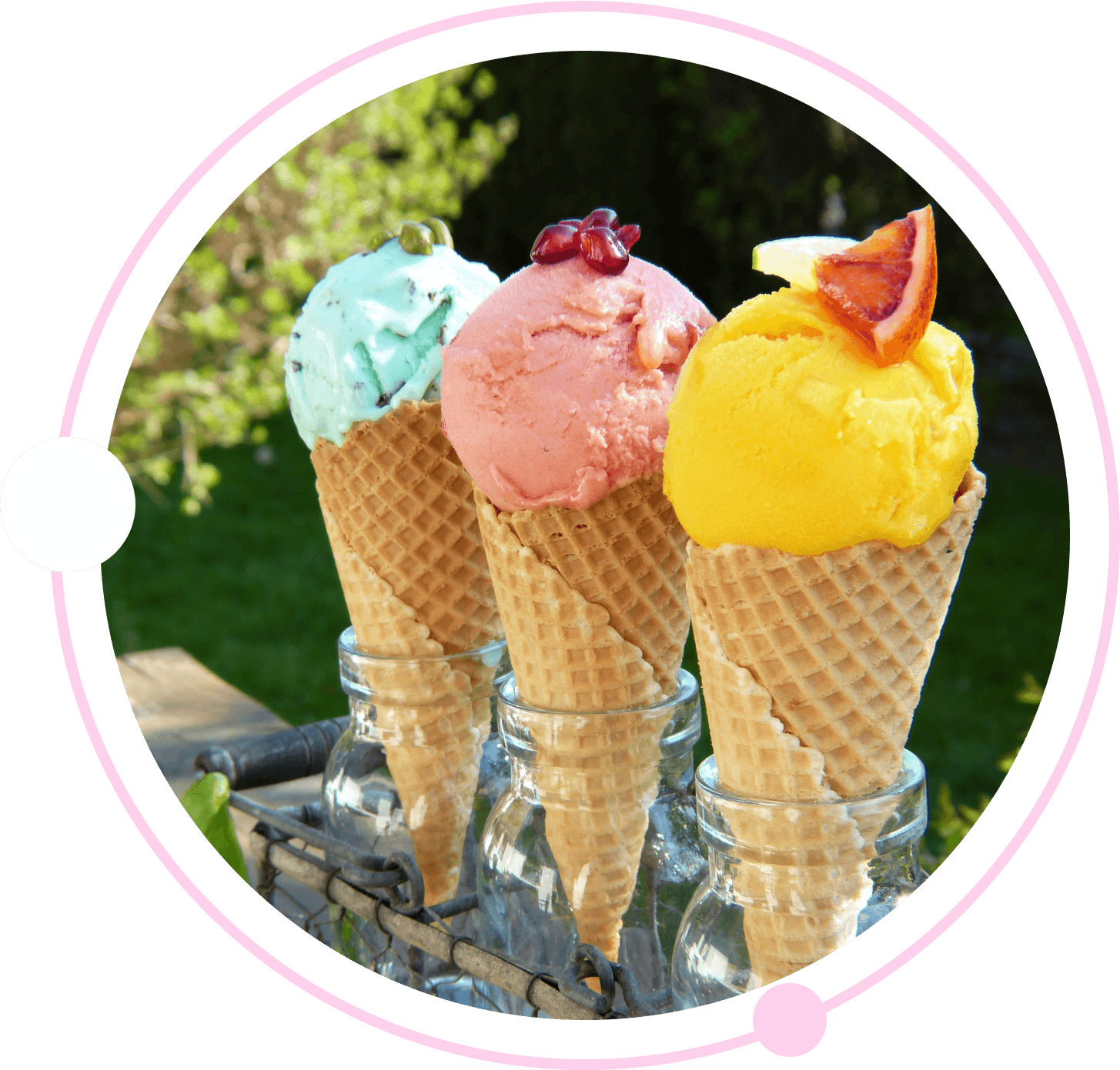 Three waffle cones with scoops of colorful ice cream (mint green, pink, and yellow) garnished with toppings, displayed outdoors in glass holders.