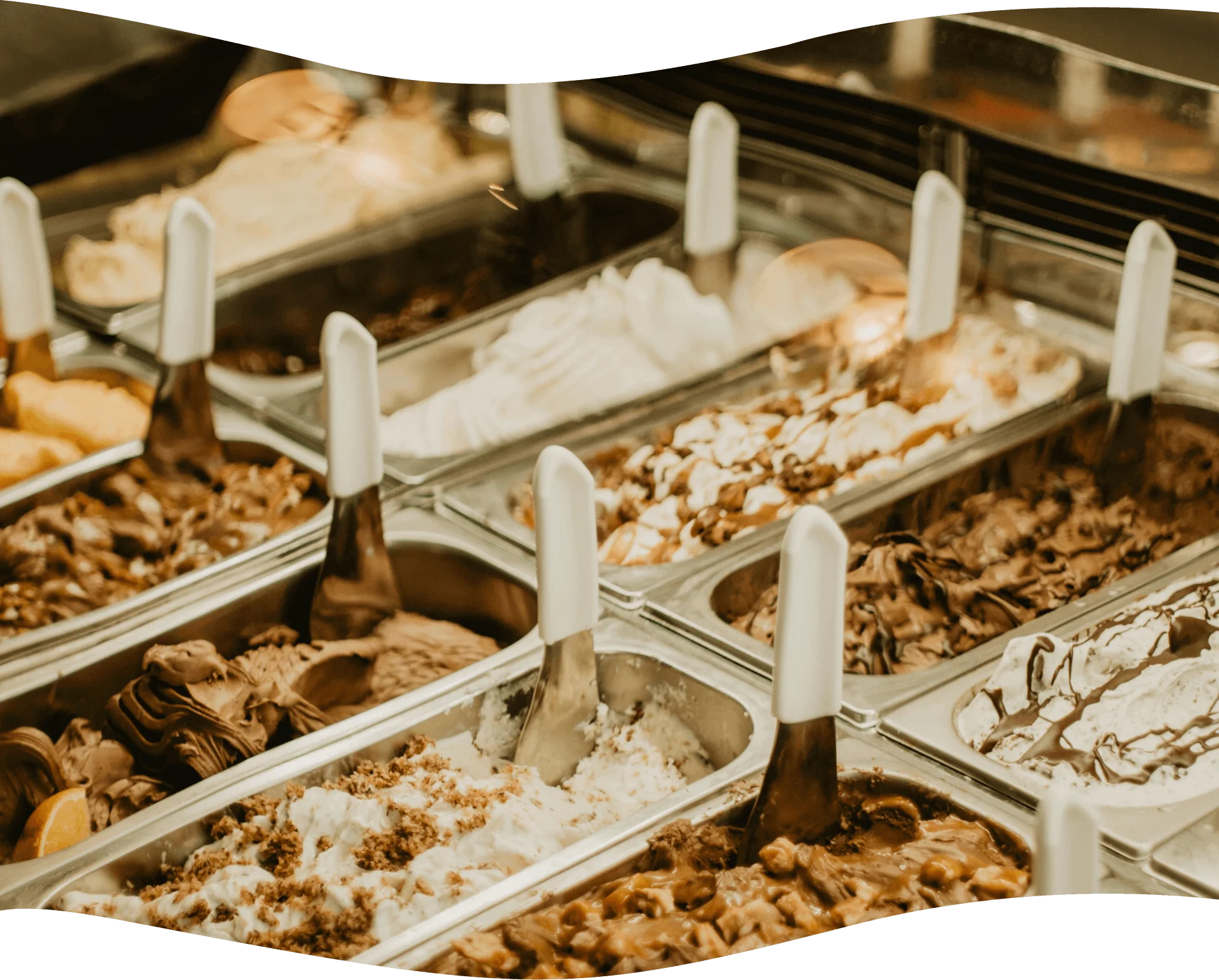 A display of various flavors of gelato in metal trays with white plastic handles, each scoop positioned upright.